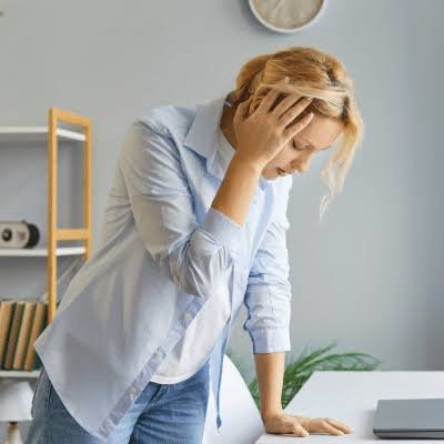 Woman leaning on desk with hand to head due to sudden dizziness and vertigo at Center of ENT Lahore