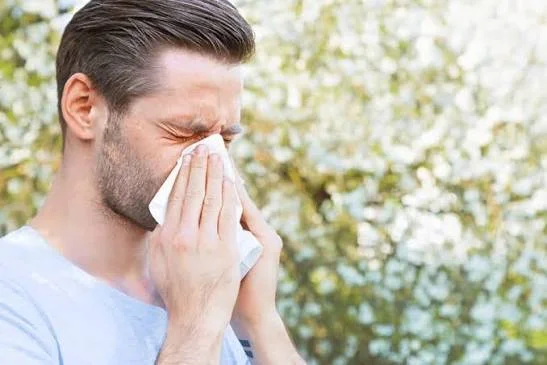 Man blowing nose with tissue outdoors experiencing pollen allergy and allergic rhinitis symptoms at Center of ENT Lahore
