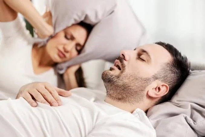 Man snoring loudly in bed while partner covers ears with pillow evaluated at Center of ENT Lahore
